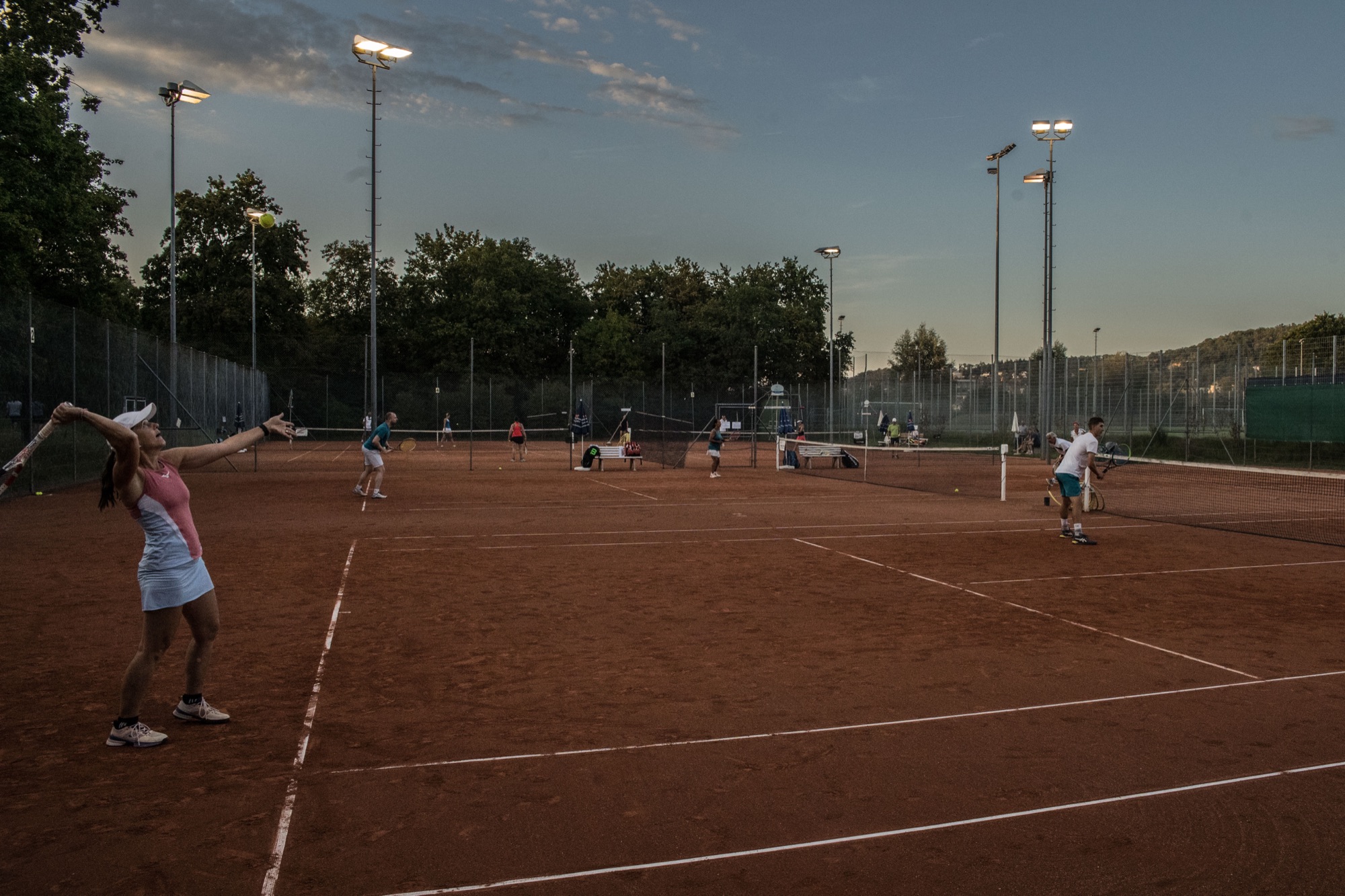 Tennisspielerinnen und Spieler bei Sonnenuntergang auf dem Sandplatz